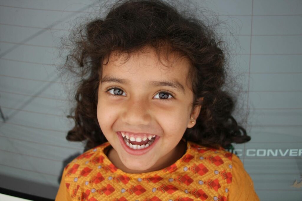 Adorable South Asian girl with curly hair, joyfully smiling outdoors.