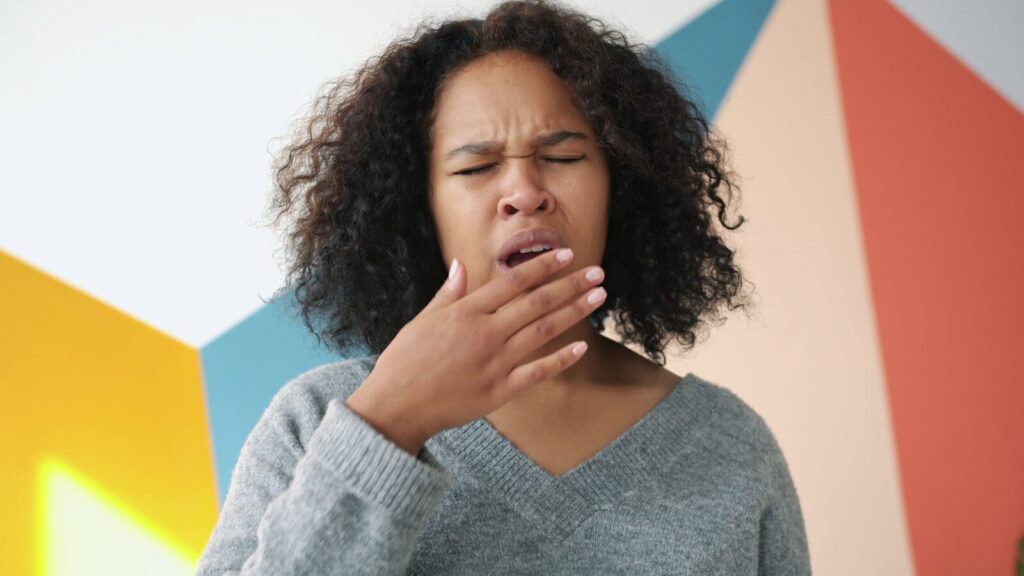 Young woman yawning with hand over mouth.