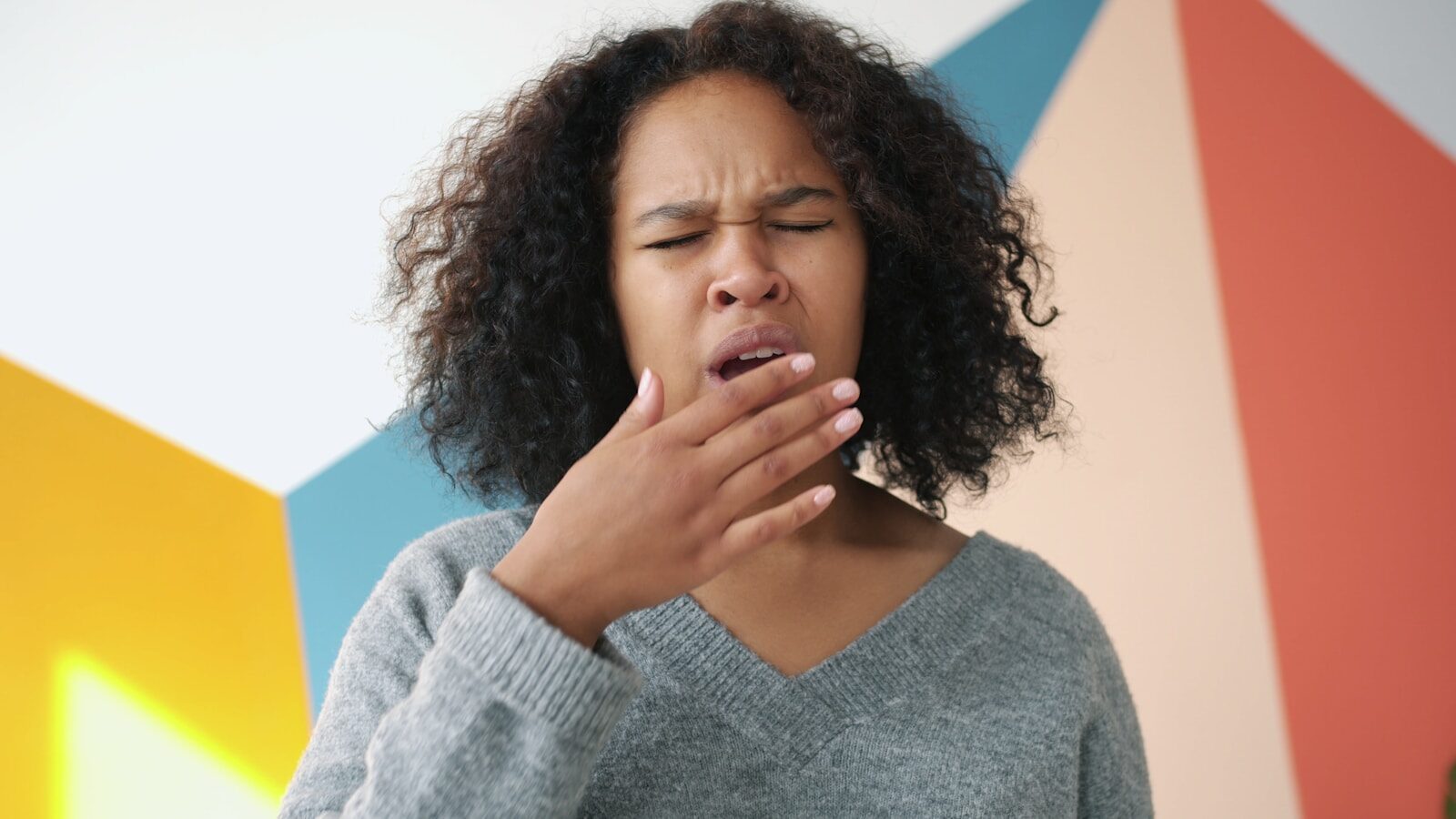 Young woman yawning with hand over mouth.